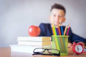 Kid in School working with pencils apple and book